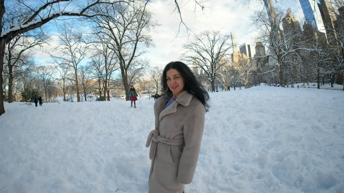 雪の公園でベージュのロングコートを着た女性