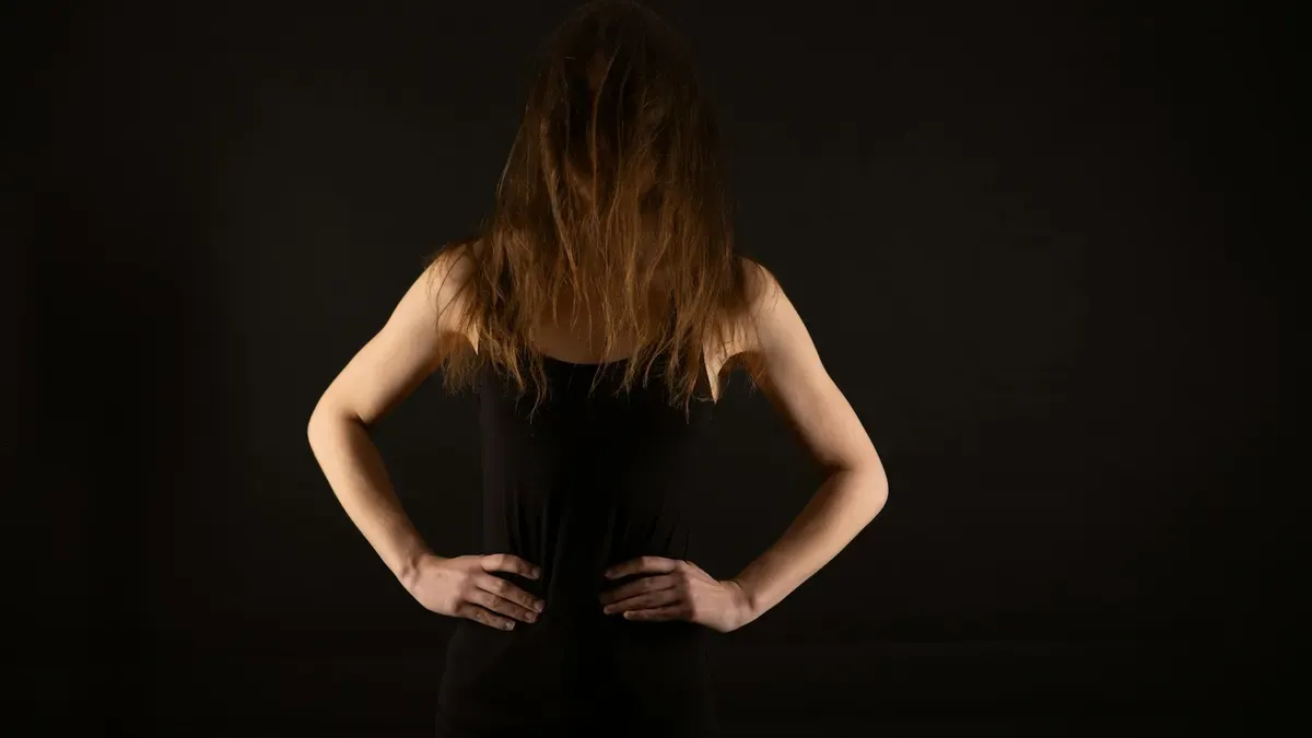 暗い背景に立つ黒髪の女性の後ろ姿