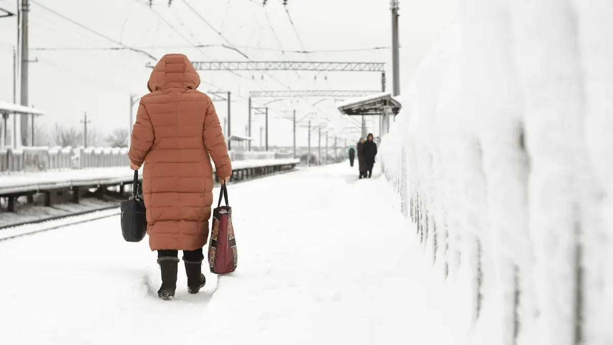 雪の駅のホームを歩くロングダウンの後ろ姿